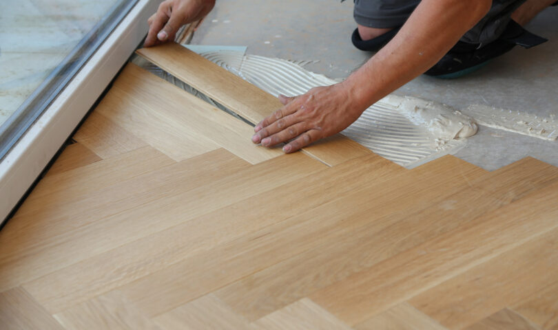 Professionele vloerenlegger installeert nauwkeurig houten visgraatvloerdelen op een gelijmde cementvloer, als voorbeeld van het vakmanschap van Vinylwood.